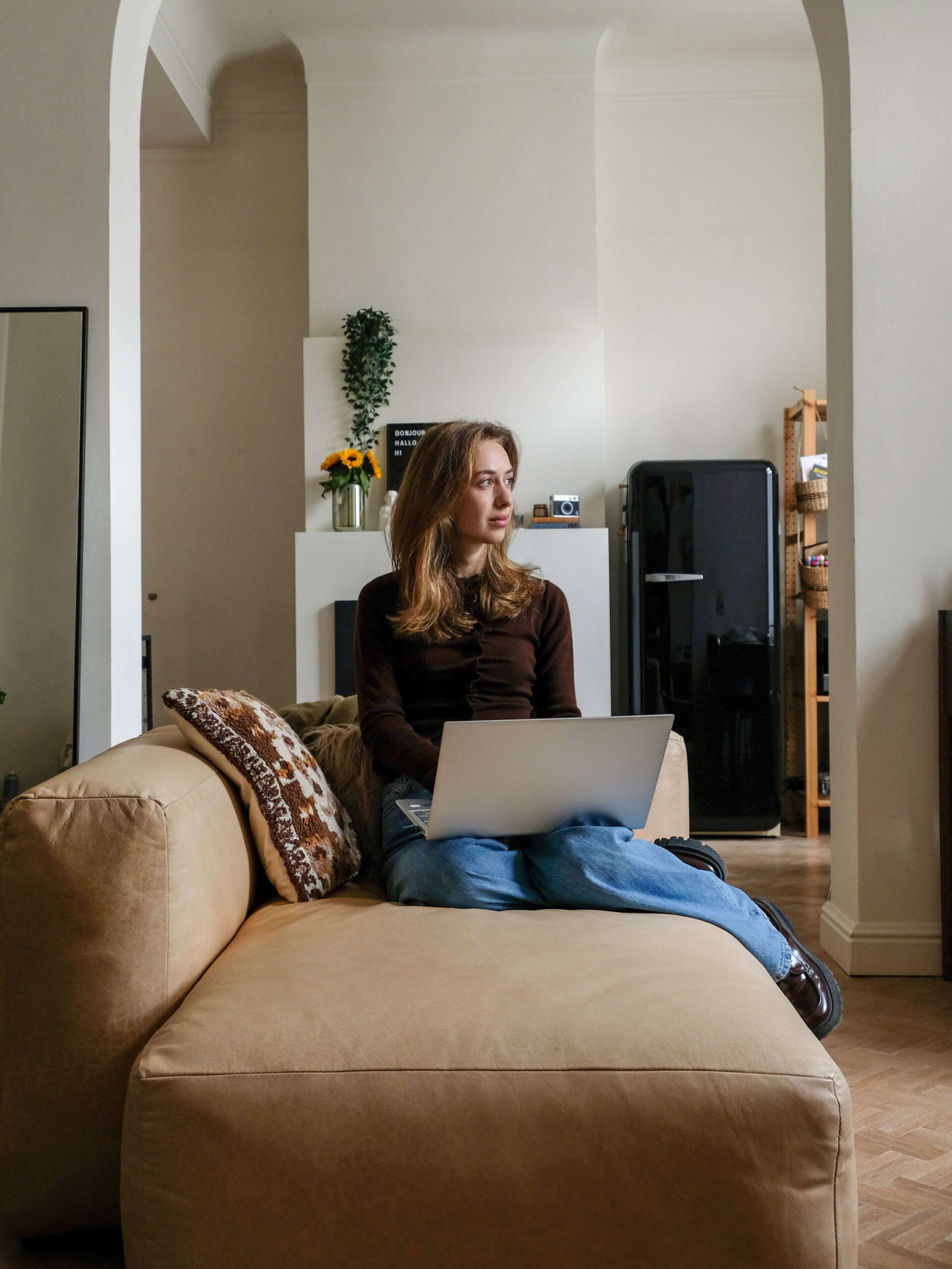 Freelance copywriter zit in bruine lederen zetel in woonkamer met laptop en kijkt naar rechts